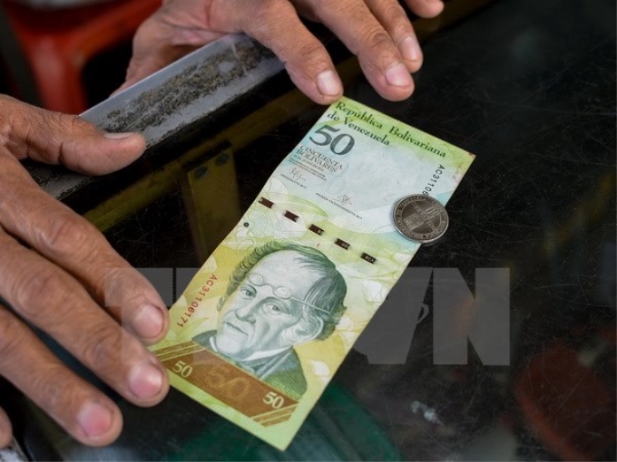 Người dân giới thiệu đồng xu 50 bolivar và tiền giấy 50 bolivar tại Caracas ngày 28/12. (Nguồn: AFP/TTXVN)