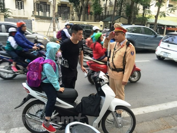 Cảnh sát giao thông kiểm tra vi phạm của phụ huynh học sinh trong việc không đội mũ bảo hiểm. (Ảnh: Việt Hùng/Vietnam+)