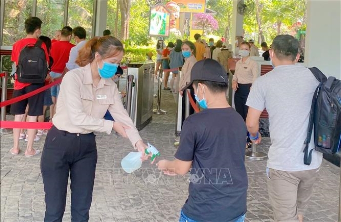 Du khách thực hiện đeo khẩu trang, xịt nước sát khuẩn trước khi vào khu du lịch Núi Thần Tài ở Đà Nẵng. Ảnh tư liệu: TTXVN phát